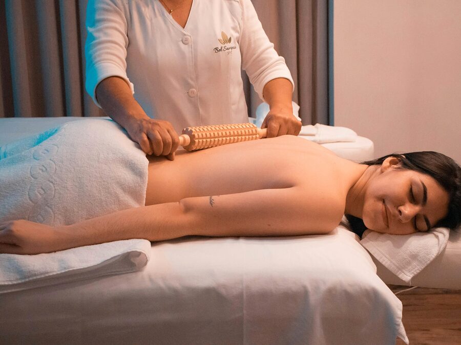 Terapeuta a massajar as costas de uma cliente com um rolo de madeira modelador