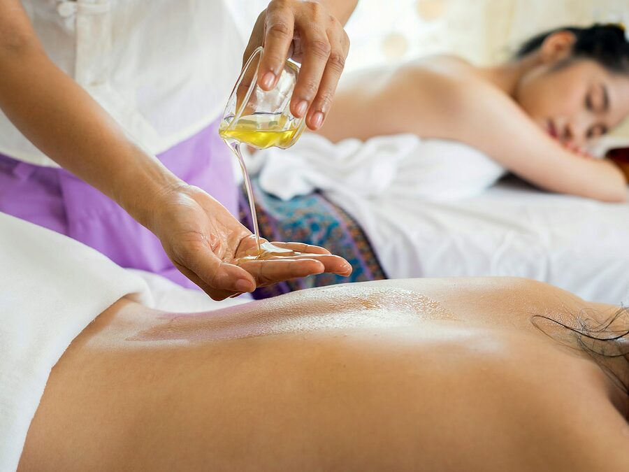 Terapeuta a deitar óleo nas mãos antes de massajar as costas de uma cliente deitada