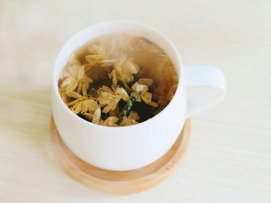 Chávena branca com infusão de flores secas sobre uma base de madeira, num fundo claro