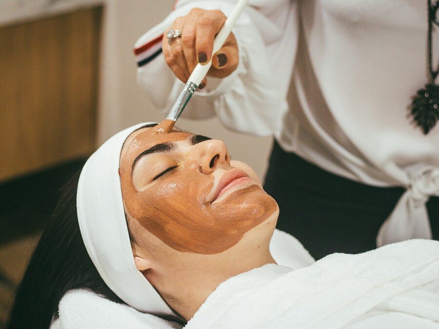 Esteticista a aplicar com pincel uma máscara facial numa cliente deitada